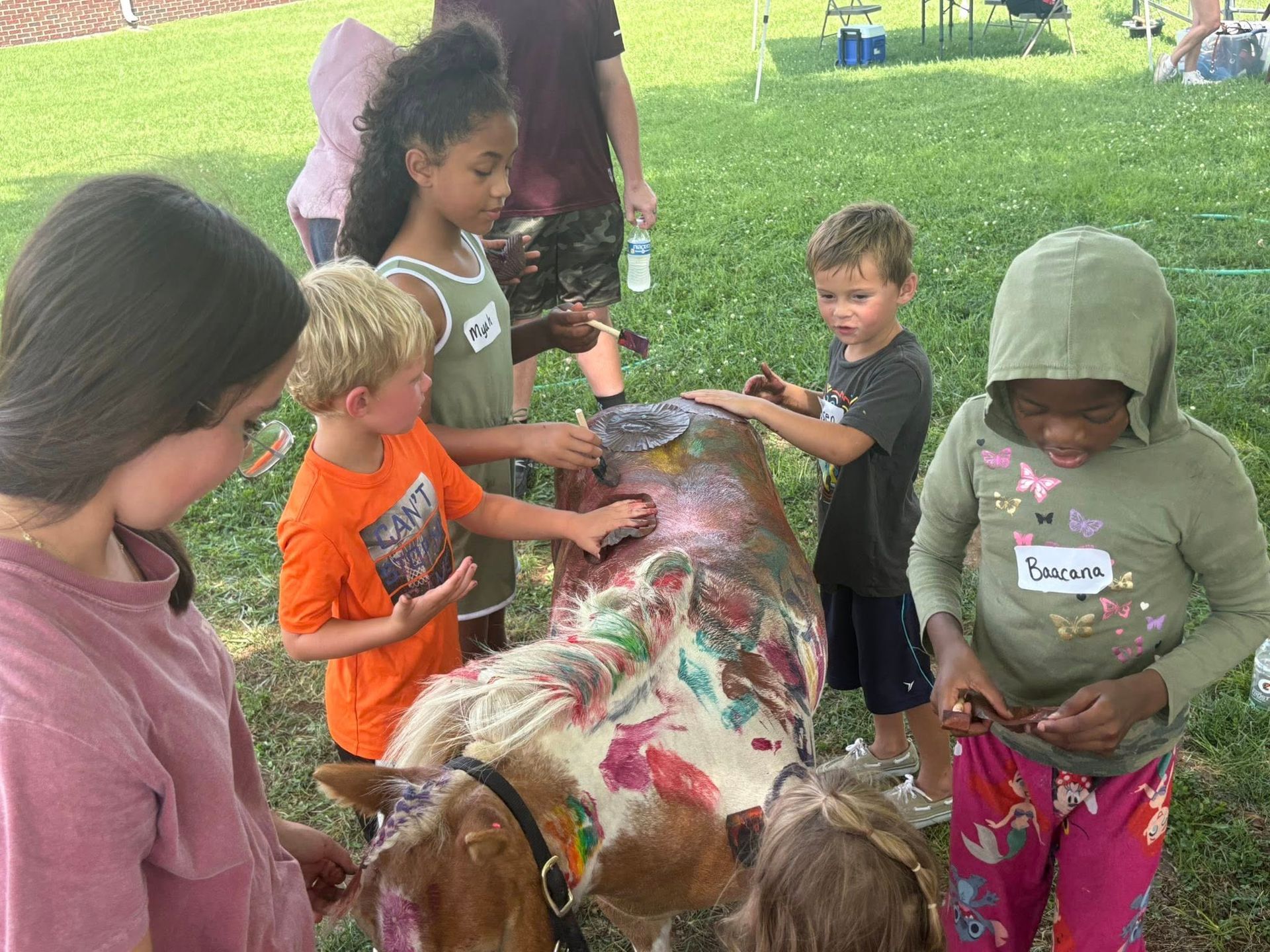 A group of children are painting a goat in a park.