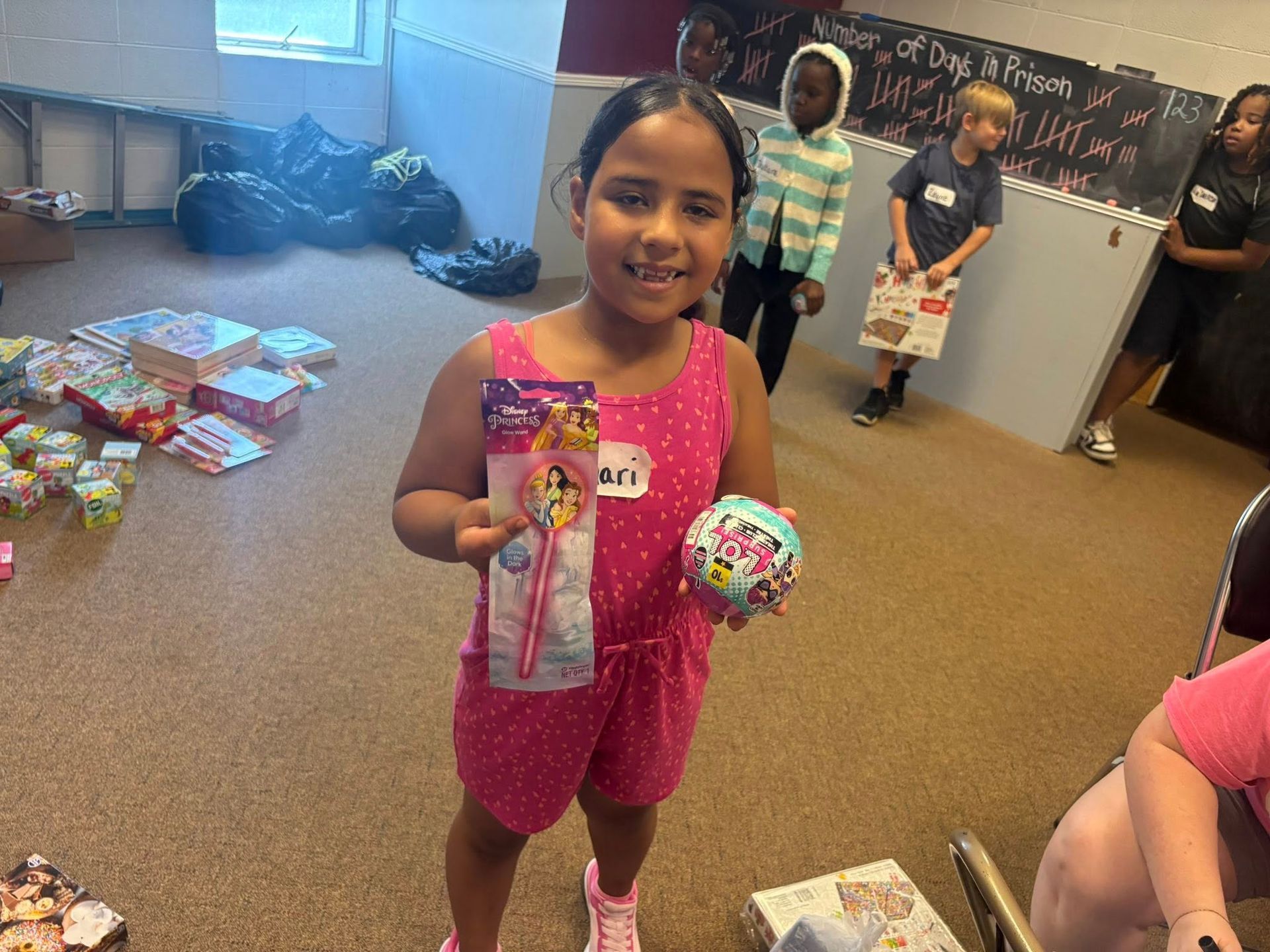 A little girl in a pink jumpsuit is holding two toys in a room.