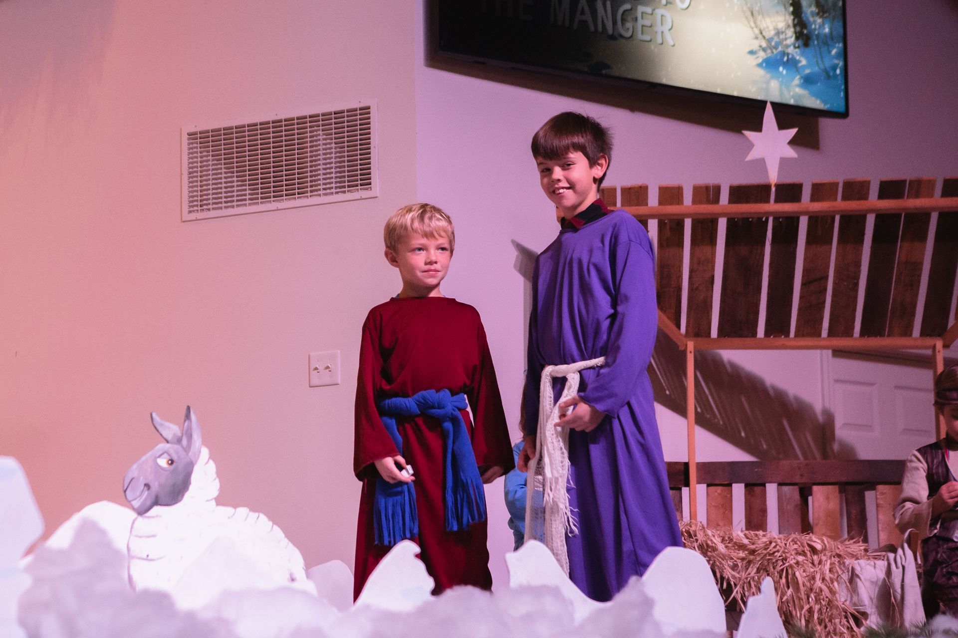 Two boys in robes stand on stage, performing in a nativity play.