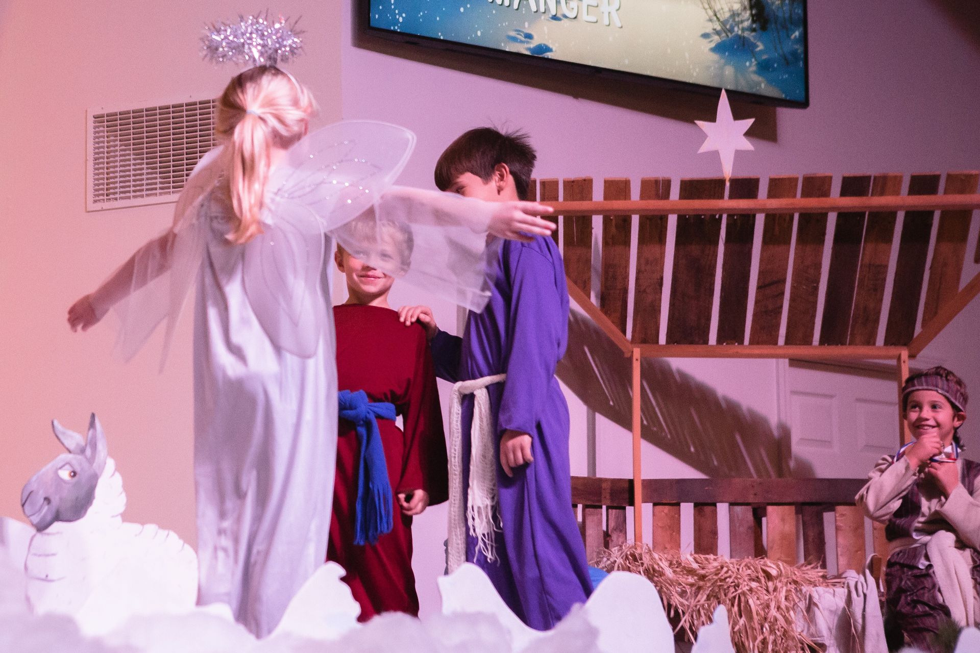 Children performing a nativity play; angel, shepherds, and Mary in costumes on stage.