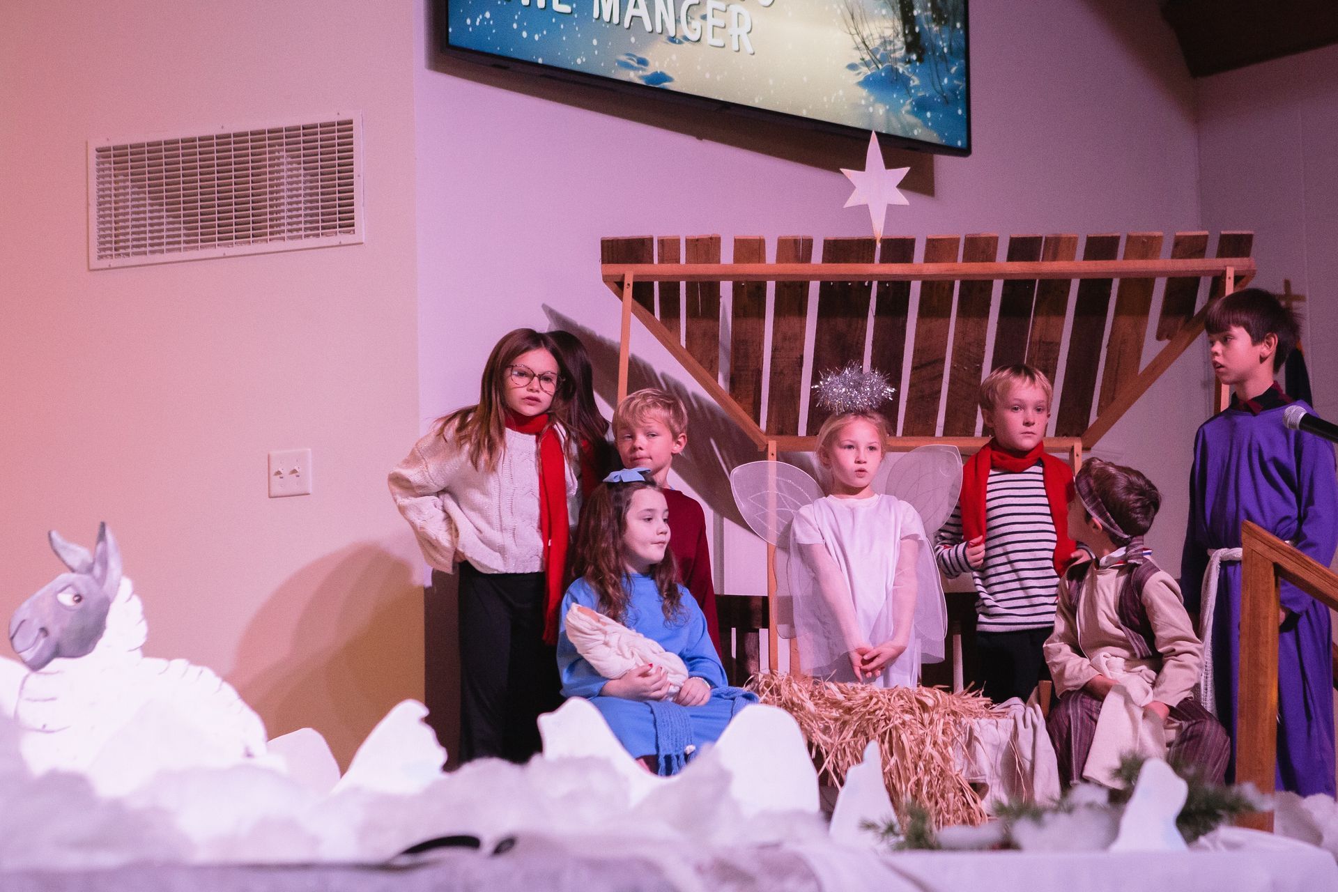 Children in costumes performing a nativity scene on a stage with a manger.
