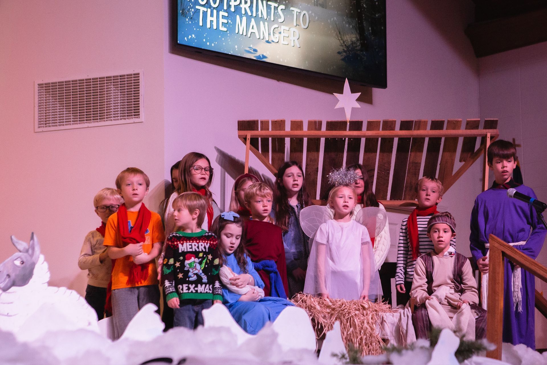 Children in nativity play on stage; manger scene, costumes, singing, Christmas.
