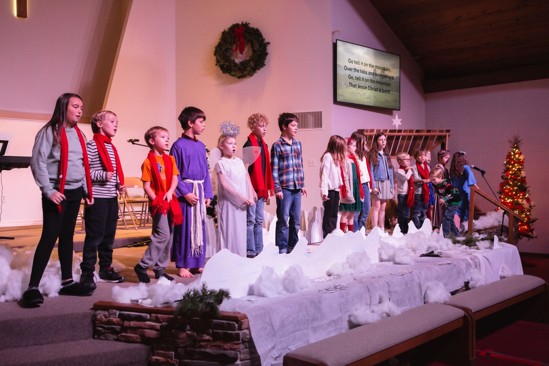 Children in a Christmas play on stage, wearing festive attire.