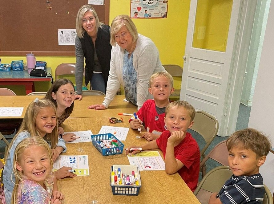 A group of young boys sitting on the floor in a line, with an orange cone nearby.
