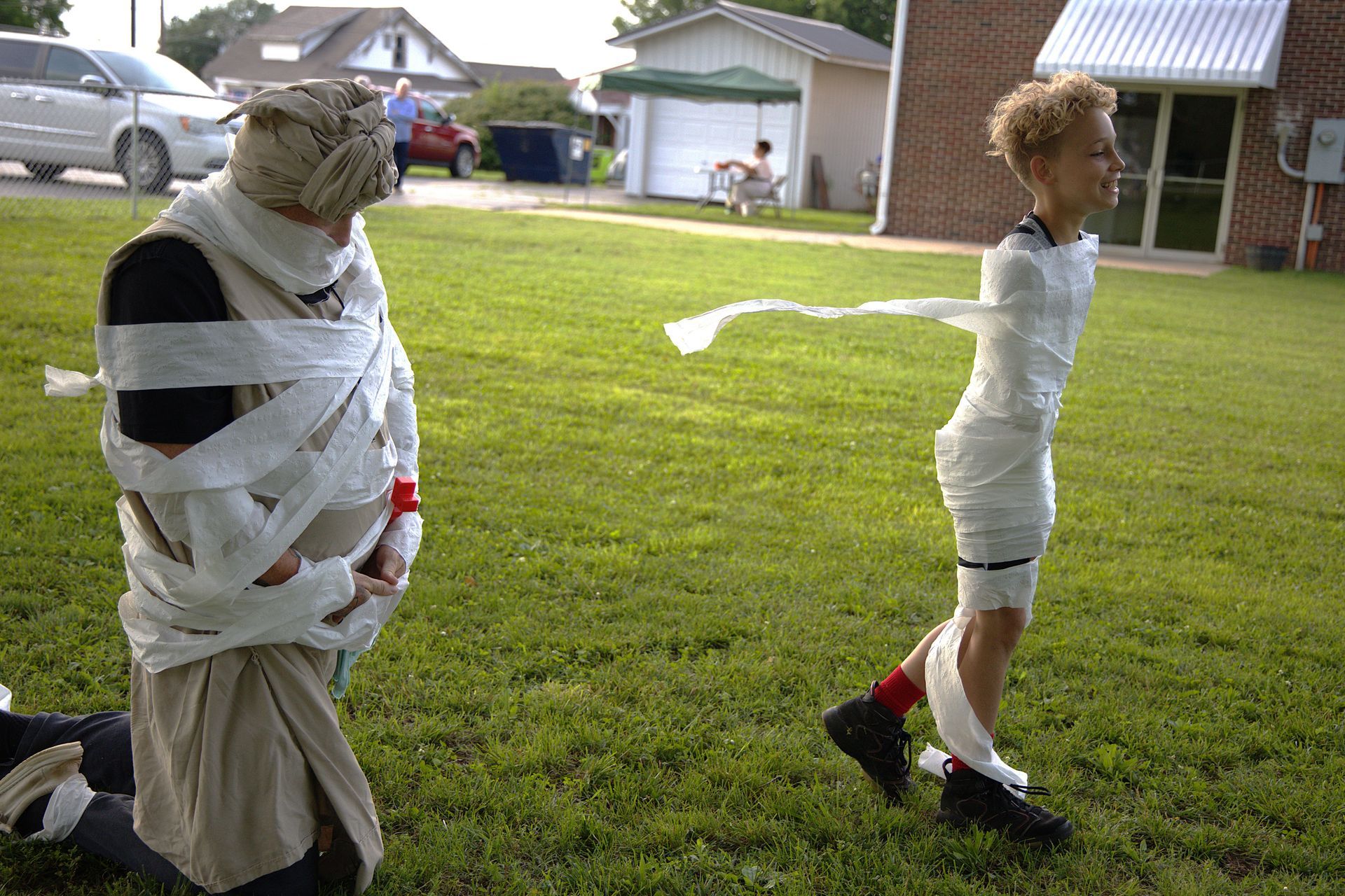 A man and a boy wrapped in toilet paper are playing in the grass