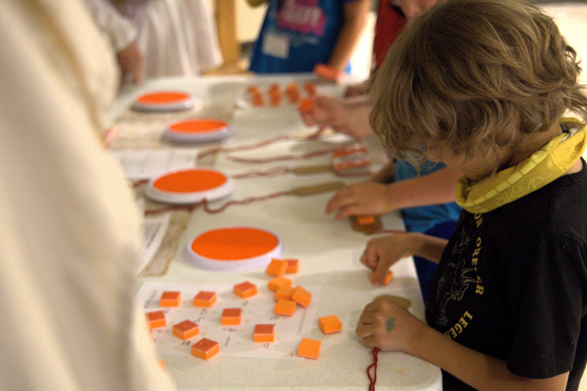 A young boy is sitting at a table playing with orange blocks.