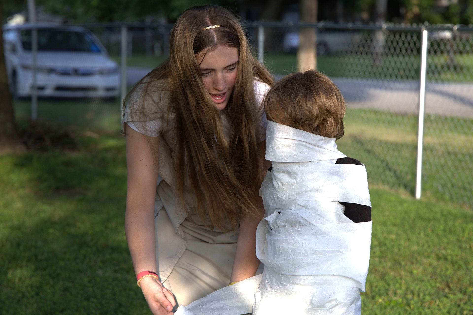 A woman is standing next to a child wrapped in toilet paper.