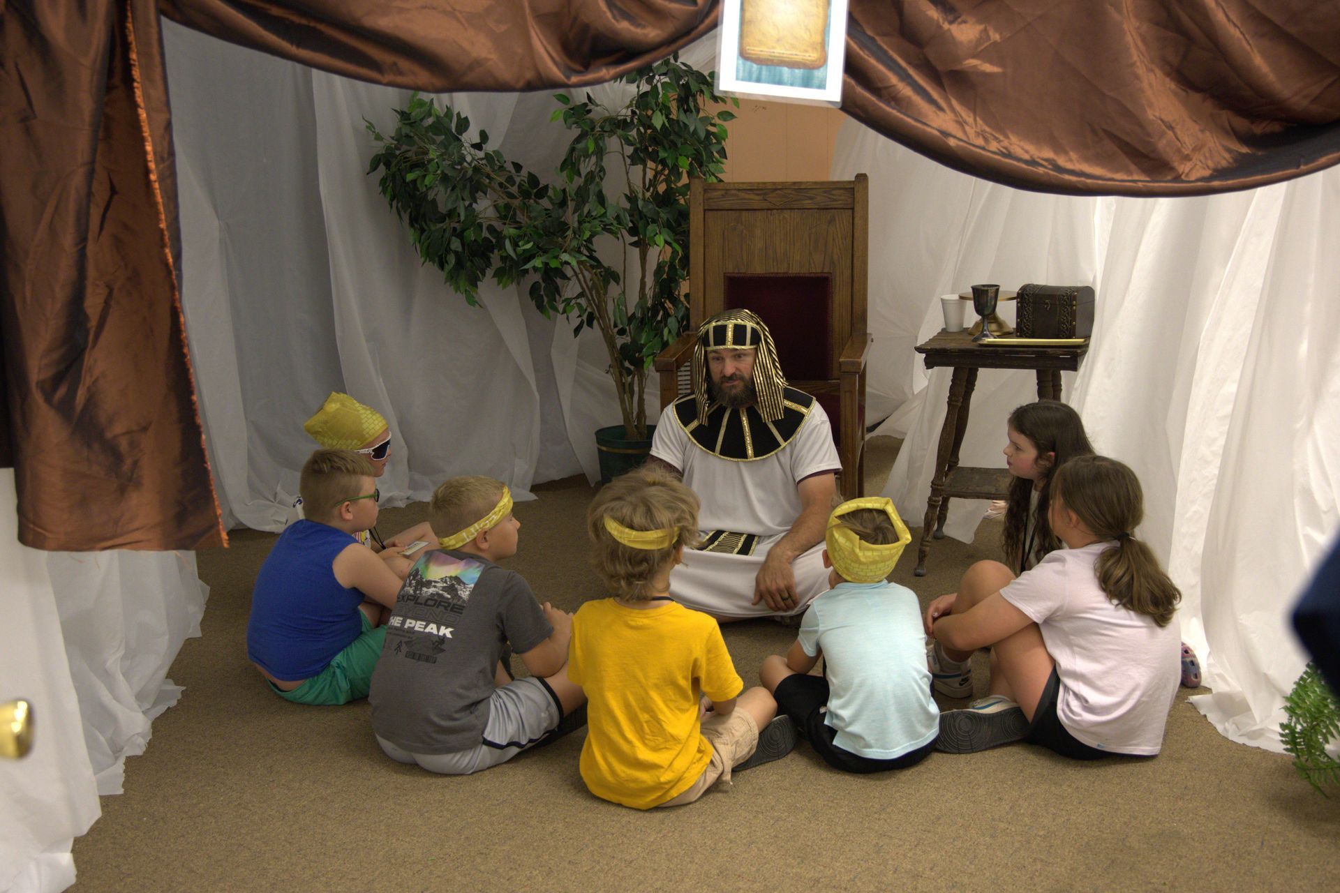 A group of children are sitting around a man in a costume.