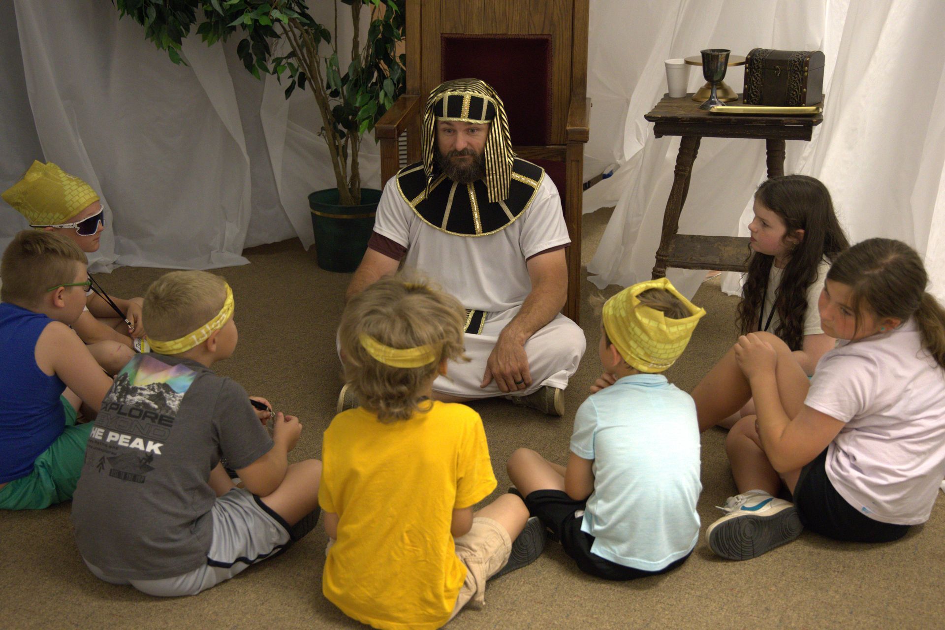 A group of children are sitting in a circle with a man sitting in the middle.