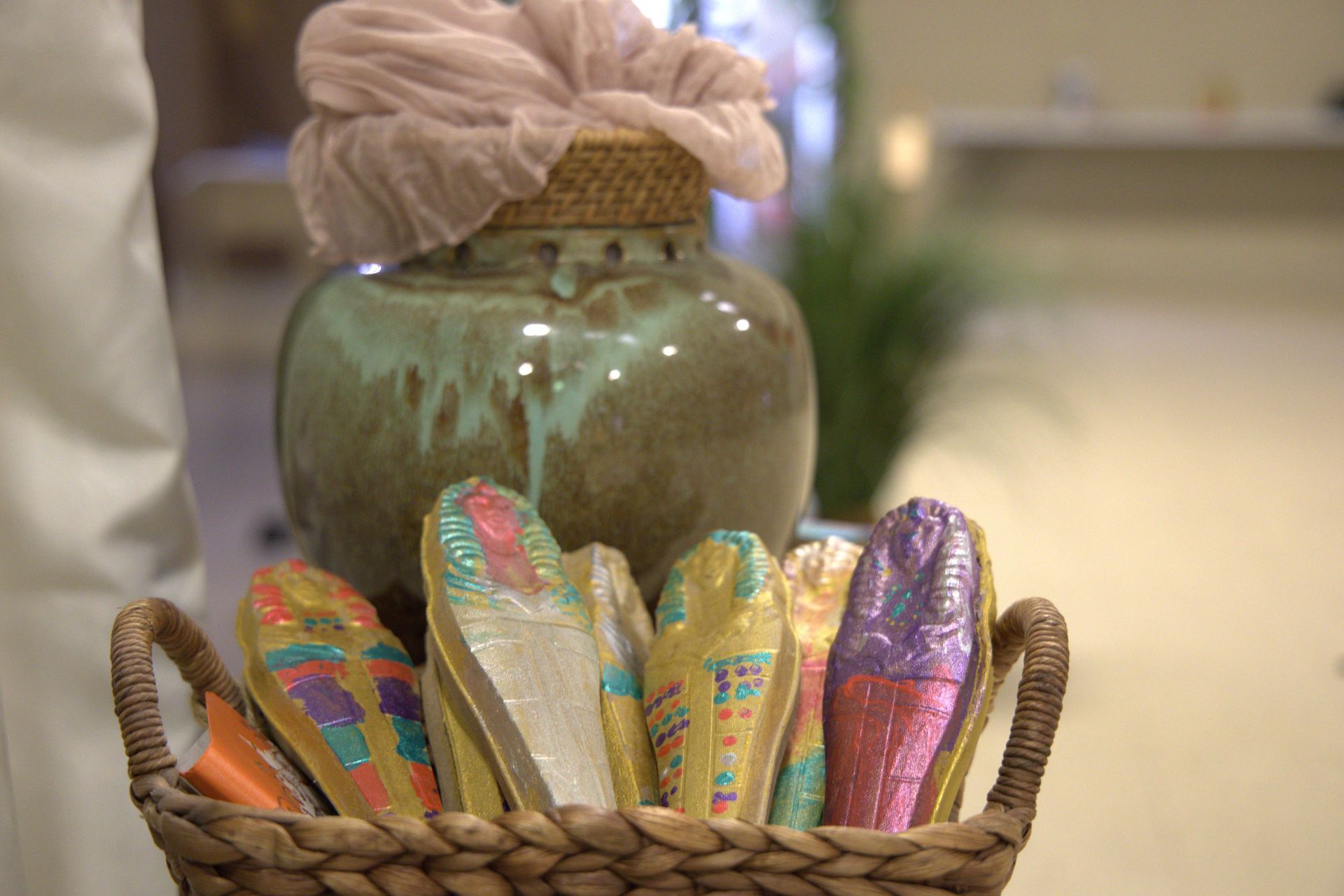 A person is holding a basket of slippers in front of a vase.