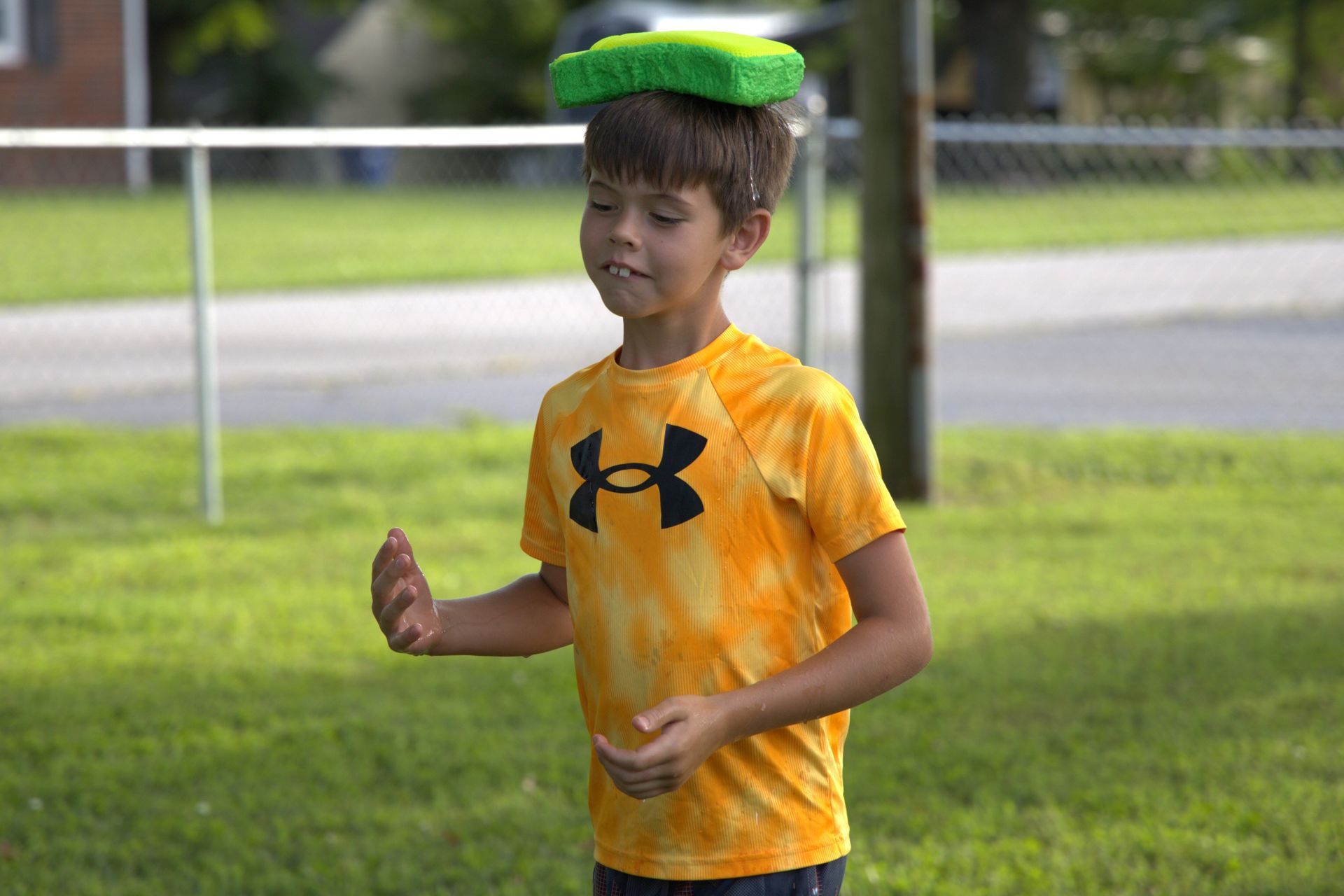 A young boy in an under armour shirt is balancing a frisbee on his head.