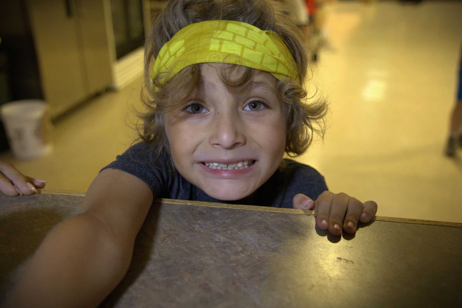 A young boy wearing a yellow headband is peeking over a counter.