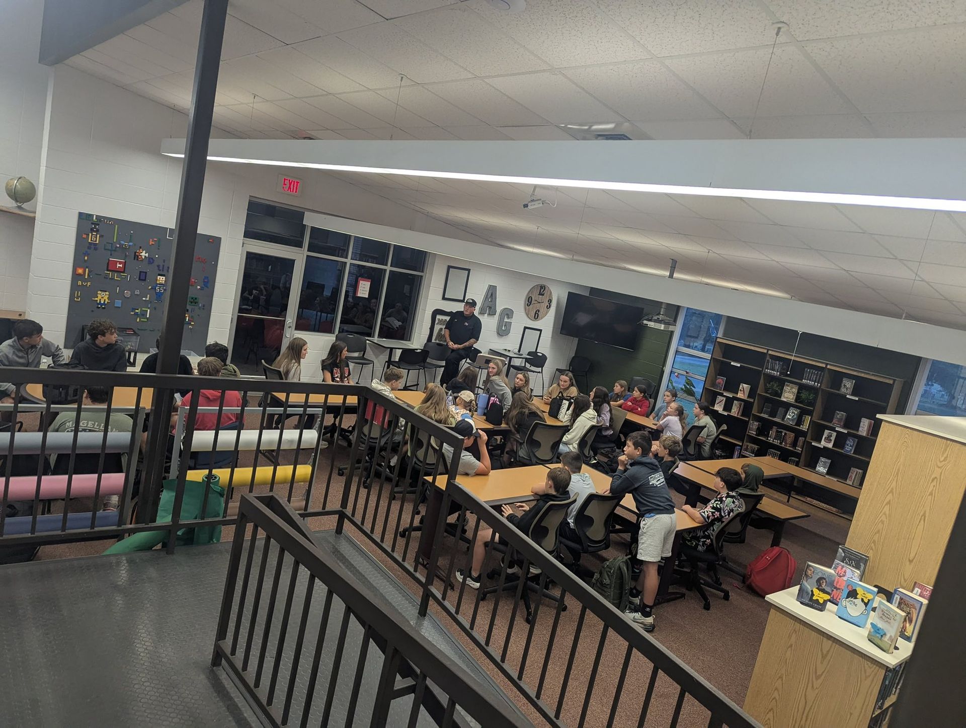 A multi-level library with students at tables, some standing, engaged in an activity.