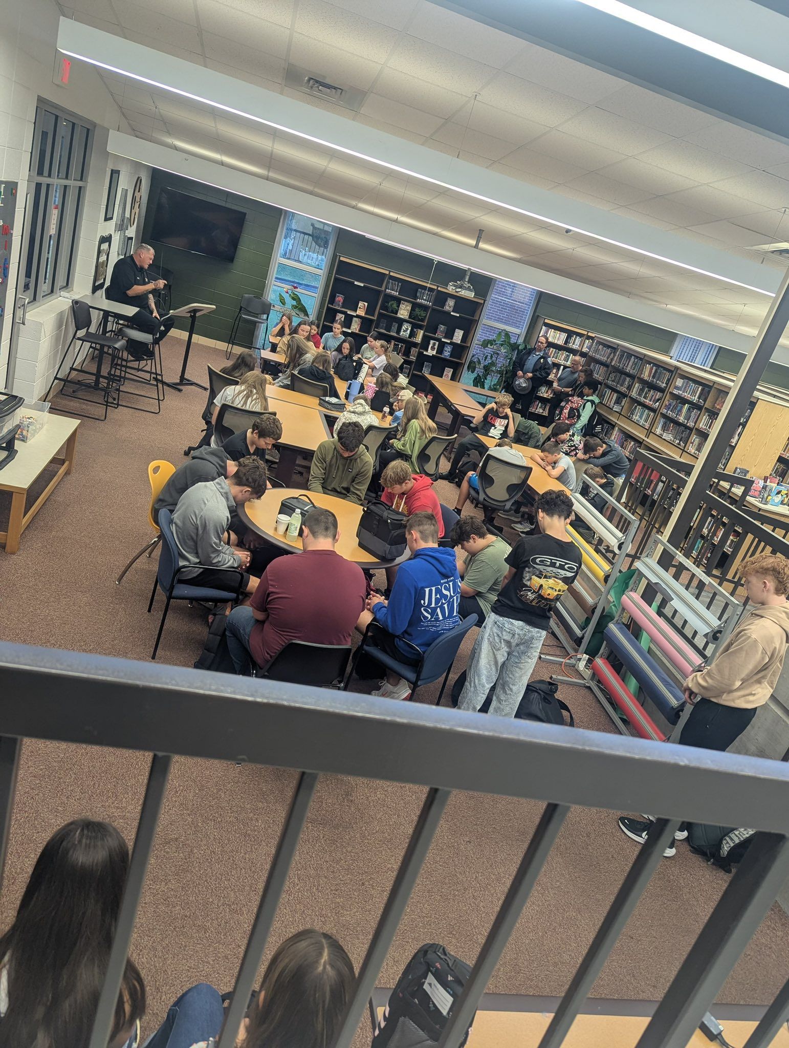Students gathered in a library; a band performs on a small stage.