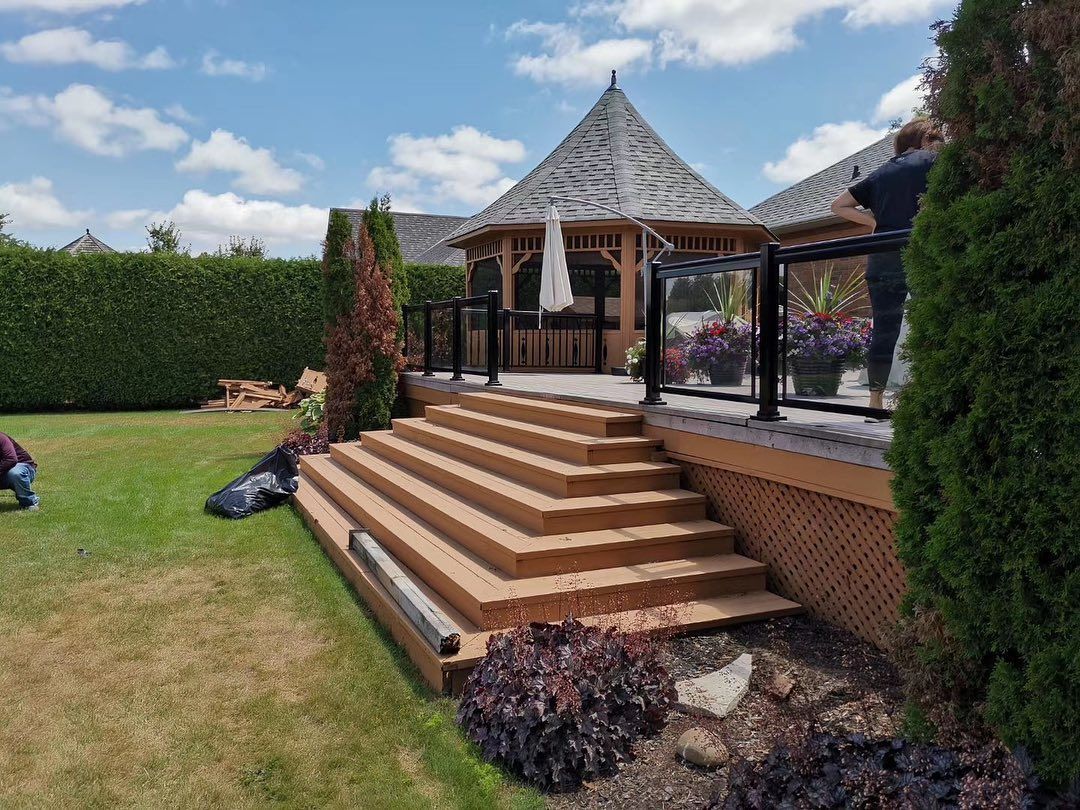 A wooden deck with stairs leading up to it and a gazebo in the background.