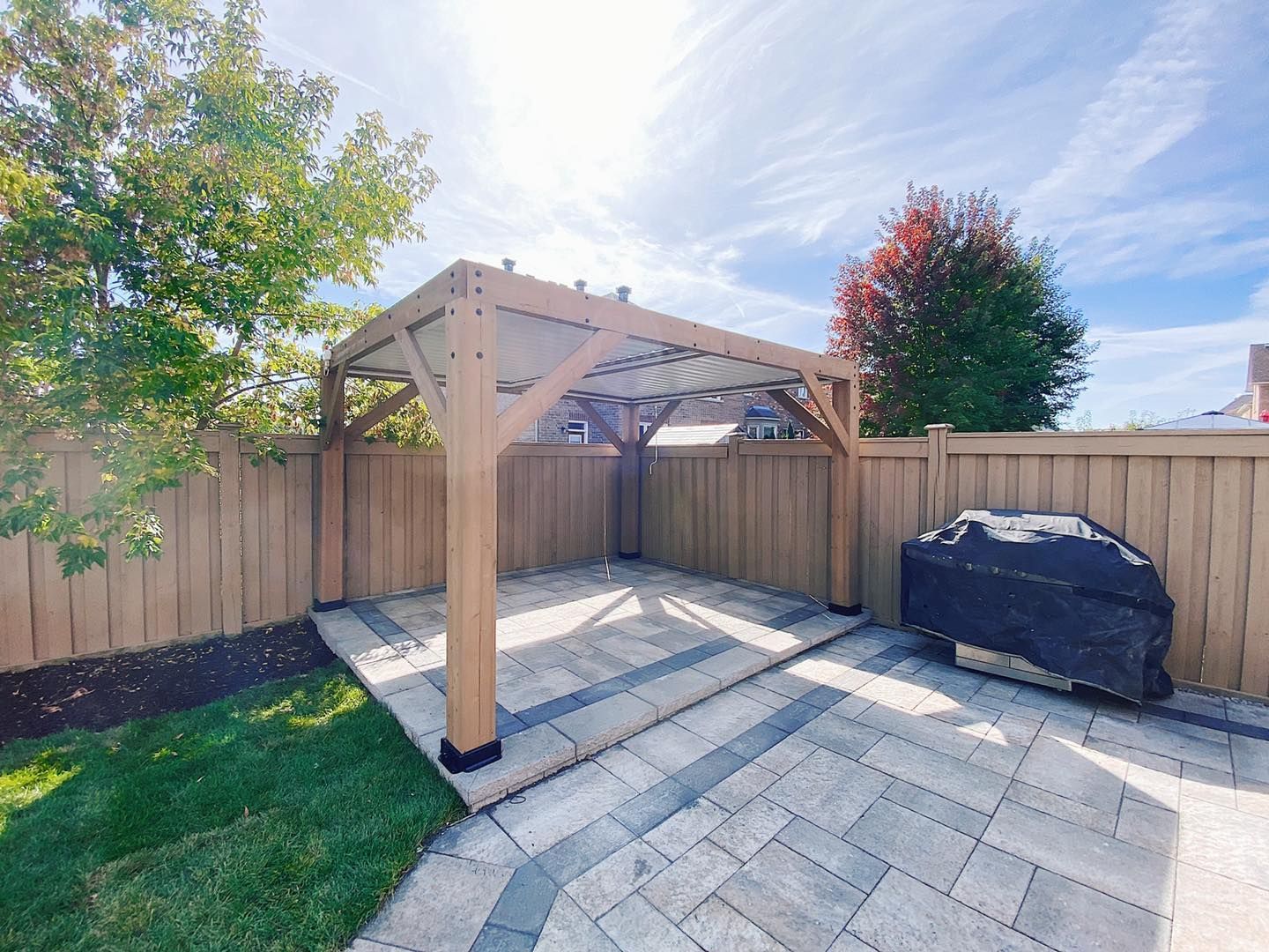 A backyard with a wooden pergola and a grill.