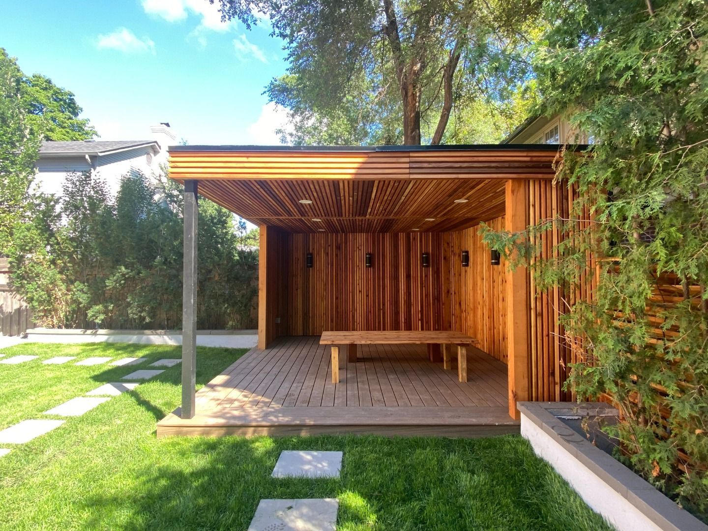 A wooden gazebo with a table and bench in the backyard