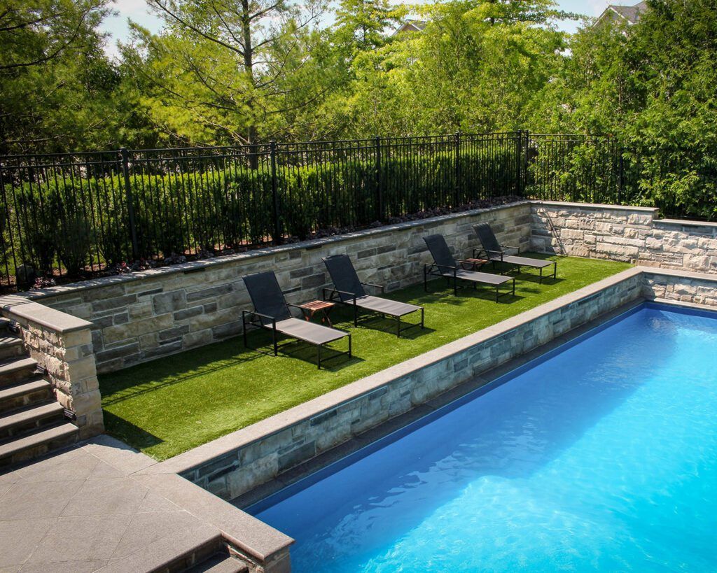 A large swimming pool surrounded by lawn chairs and a stone wall.