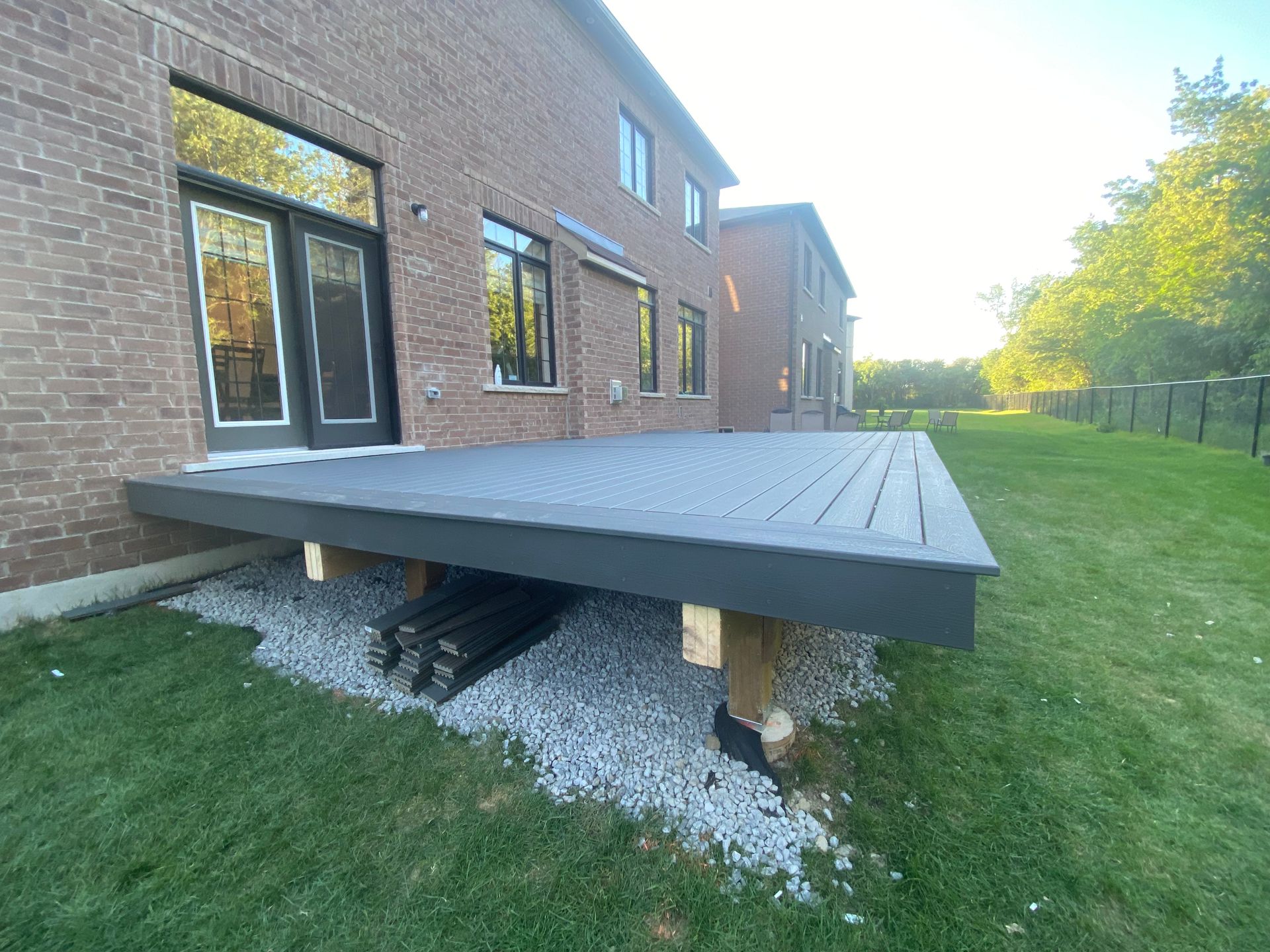 A large deck is sitting in the grass in front of a brick house.