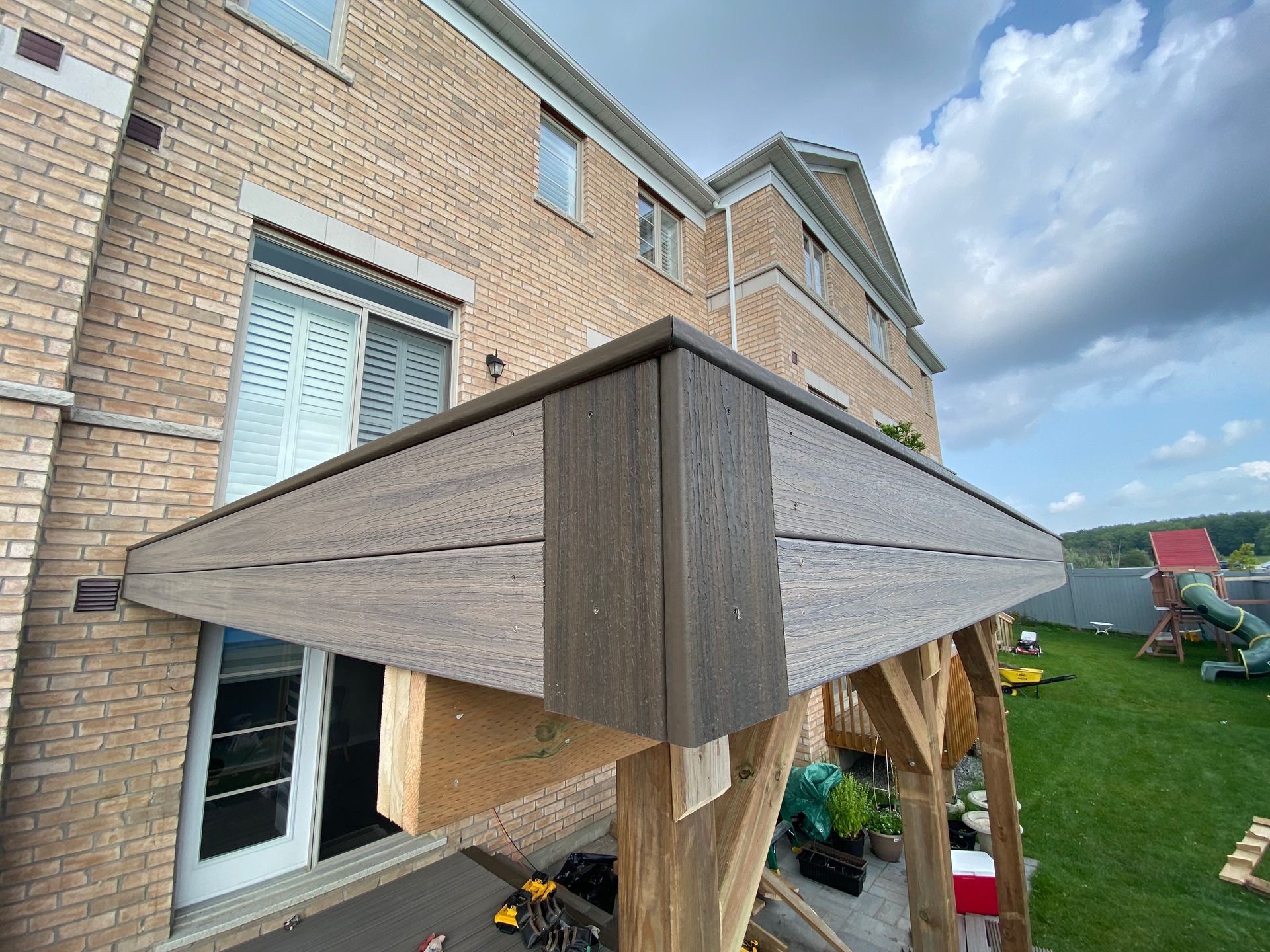 A wooden pergola is being built on the side of a brick house.