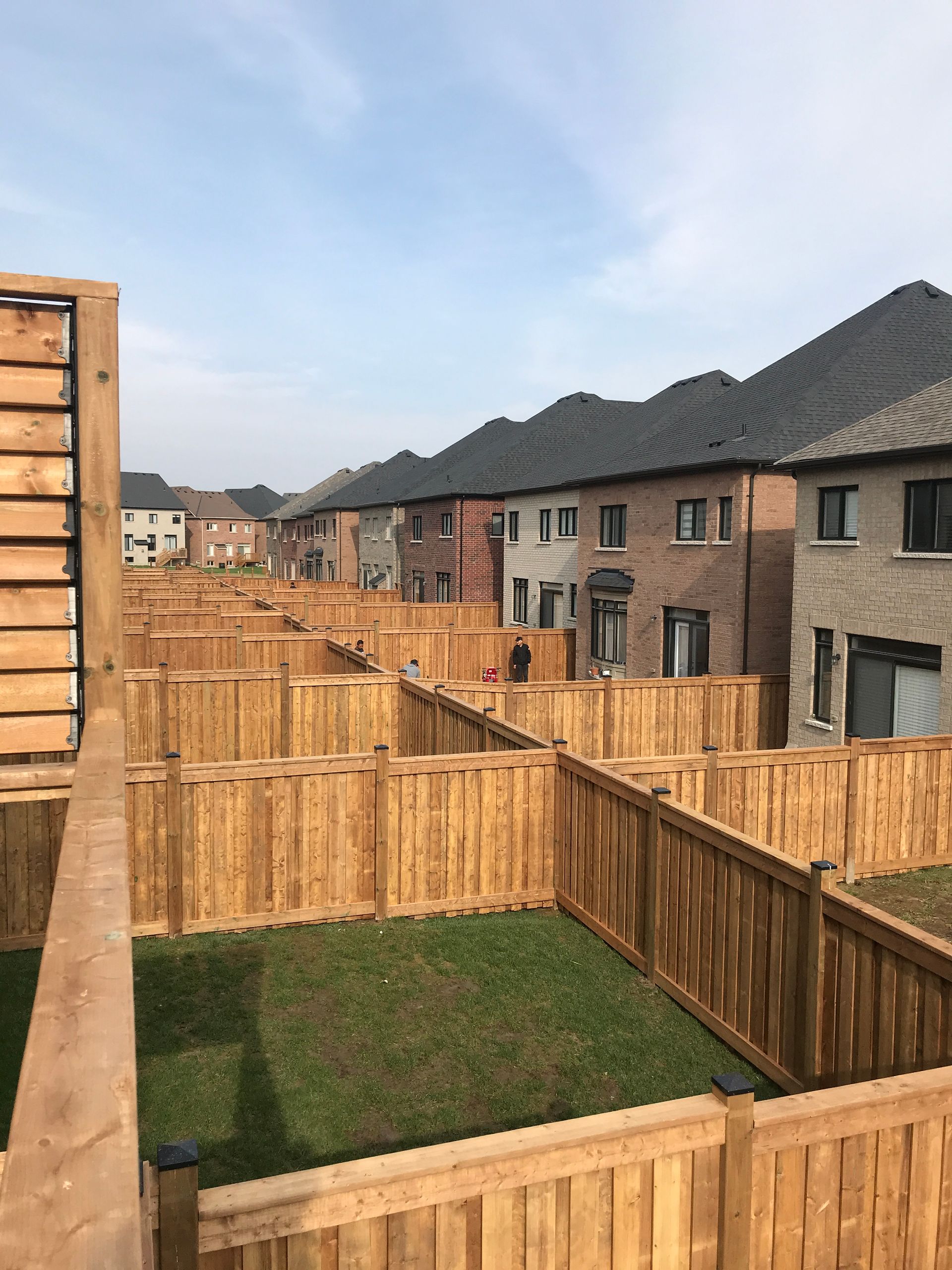 A wooden fence surrounds a lush green field in a residential area.