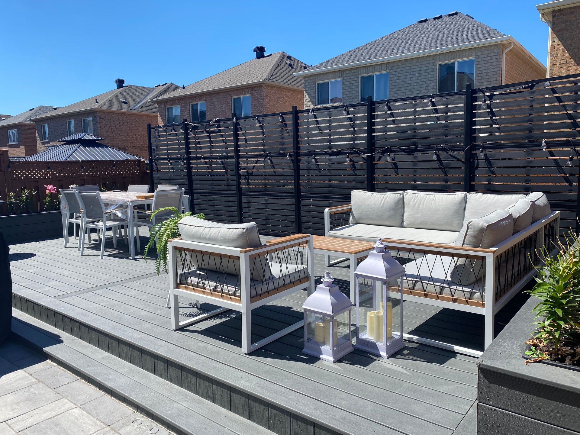 A patio with a couch , chairs , lanterns and a table.