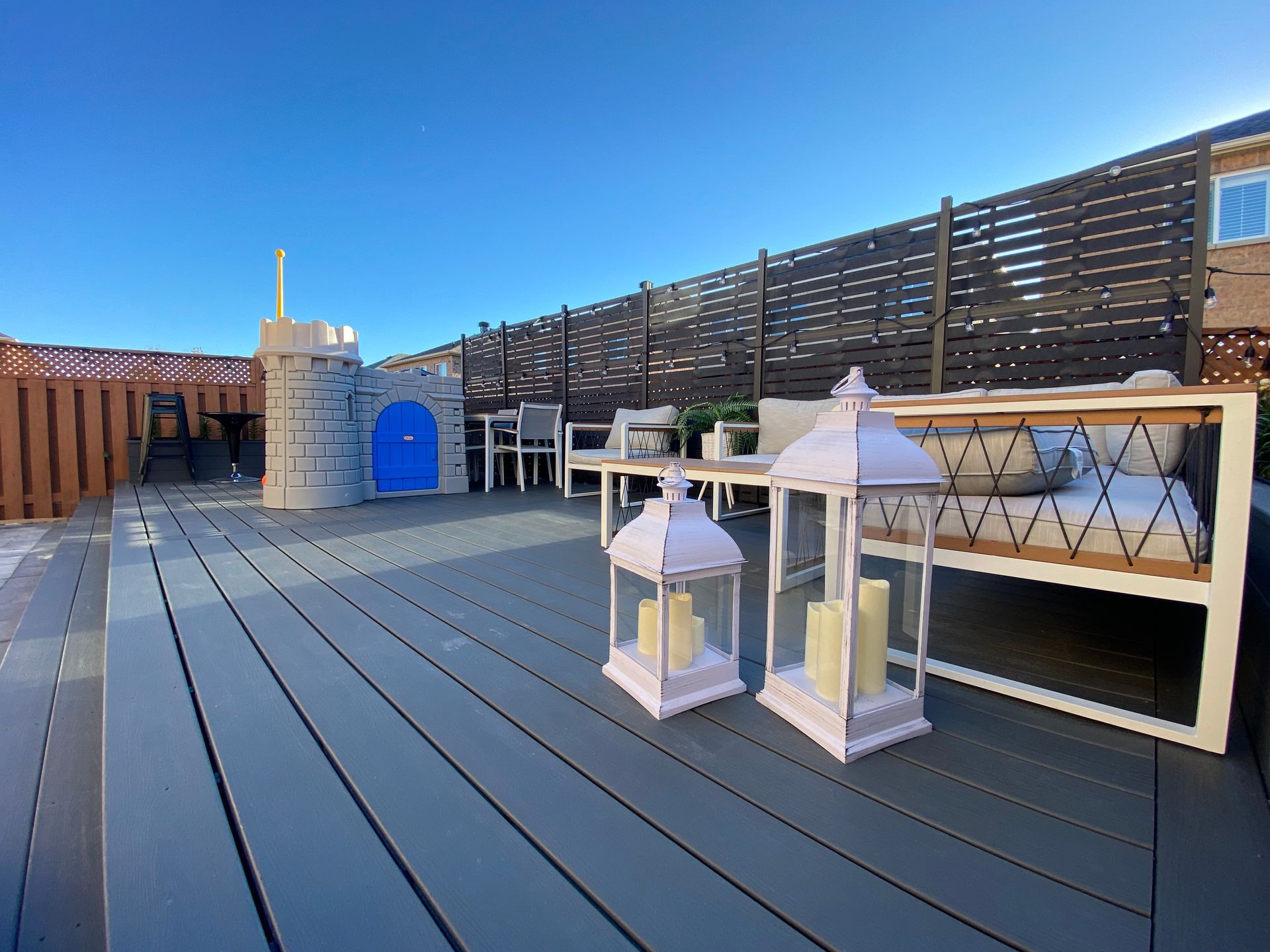 A deck with a couch , chairs , and lanterns on it.