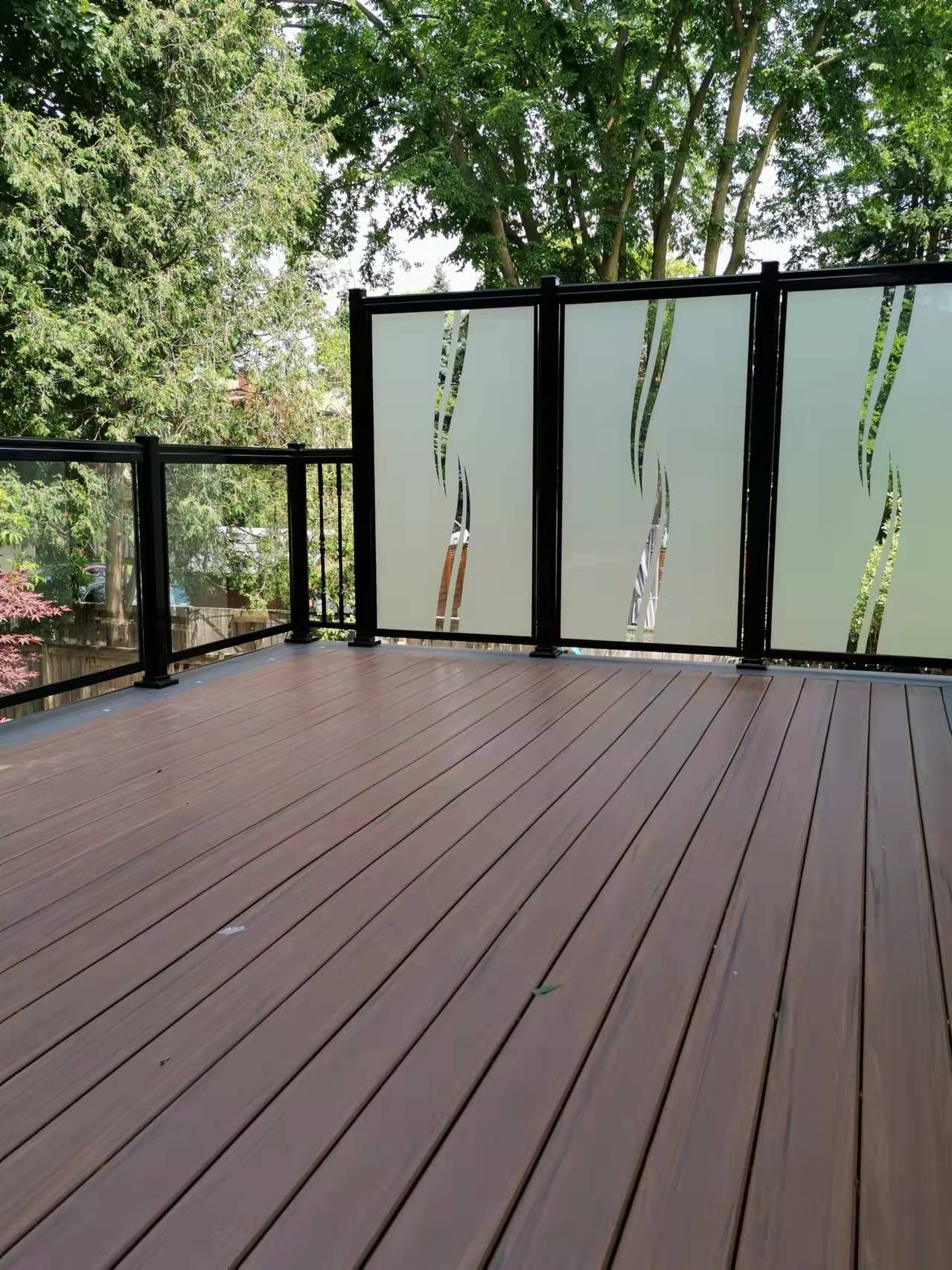 A wooden deck with a glass railing and trees in the background
