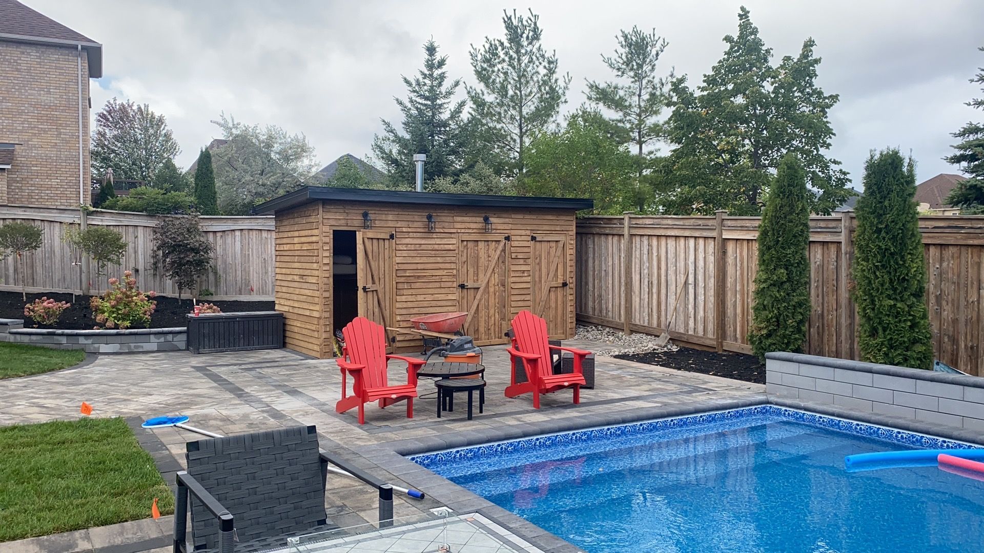 A backyard with a swimming pool , chairs , a table and a shed.