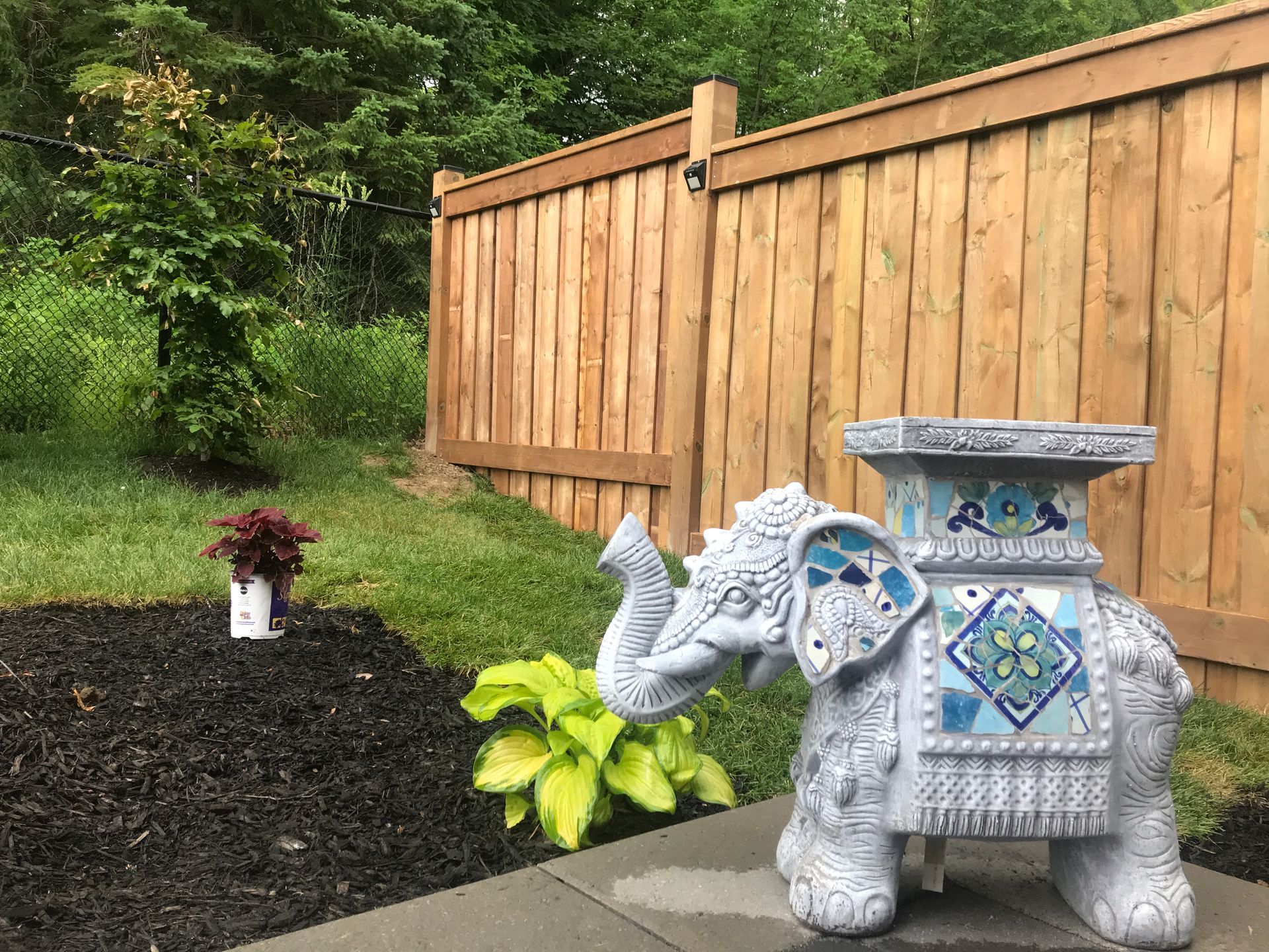 A statue of an elephant is sitting on a sidewalk in front of a wooden fence.
