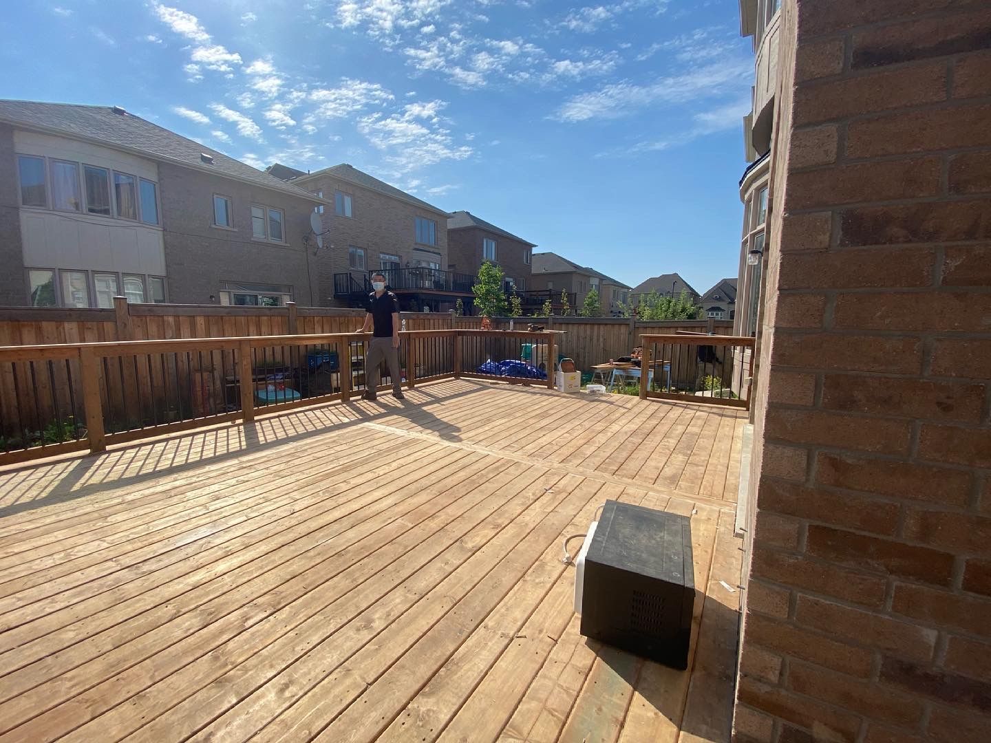A man is standing on a wooden deck in front of a brick building.