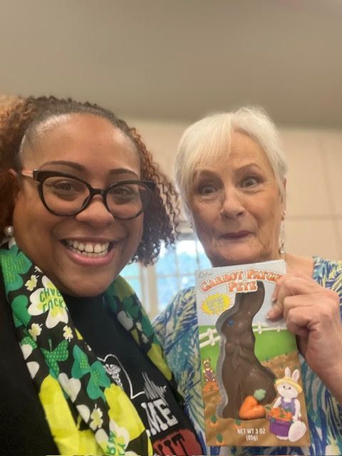 Two women are posing for a picture and one is holding a chocolate bunny.