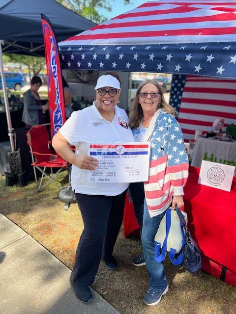Two women are standing next to each other in front of an american flag tent.
