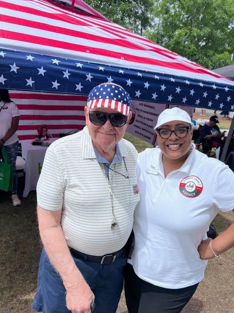 A man and a woman are posing for a picture in front of an american flag.