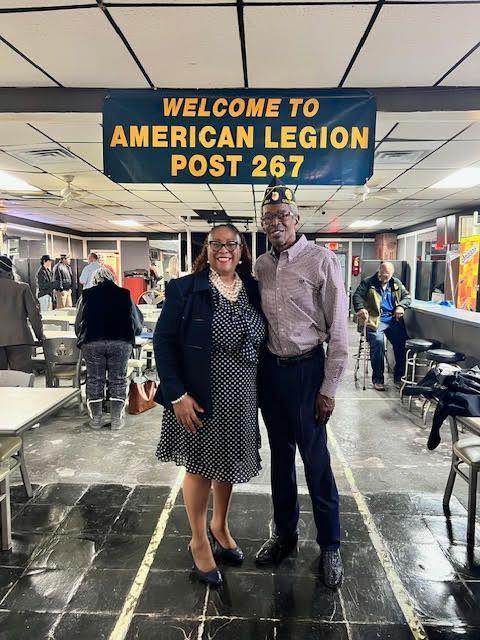 A man and a woman are standing in front of a sign that says welcome to american legion post 267.
