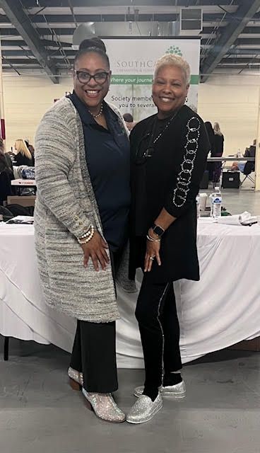 Two women are standing next to each other in front of a table.
