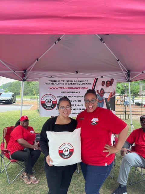 Two women in red shirts are posing for a picture under a pink tent.