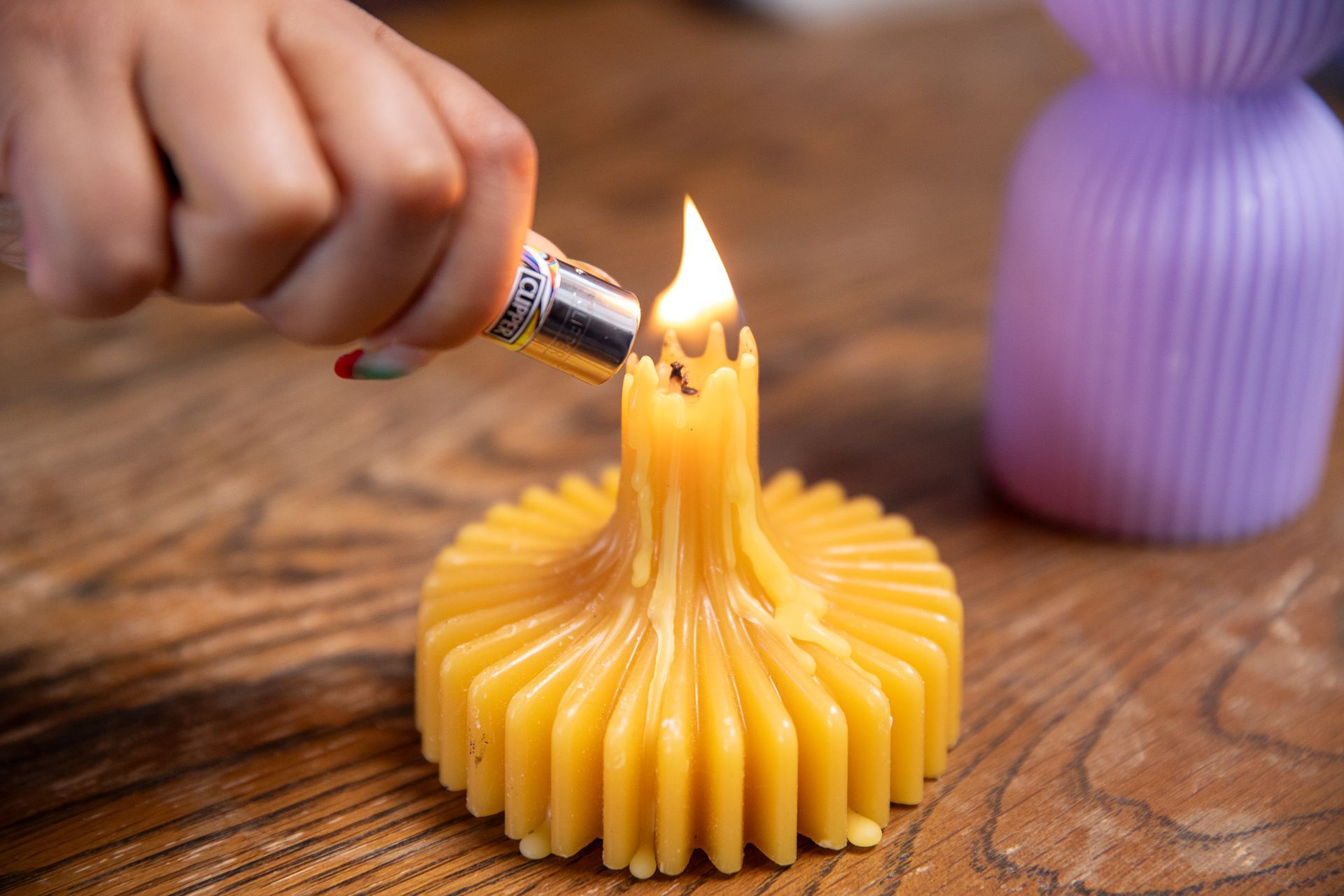 A person is lighting a candle with a lighter on a wooden table.