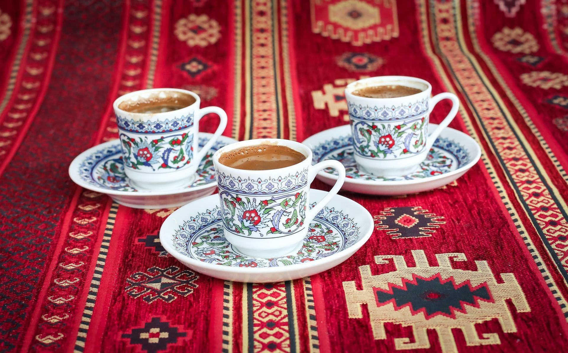 Three cups of coffee are sitting on a red rug.