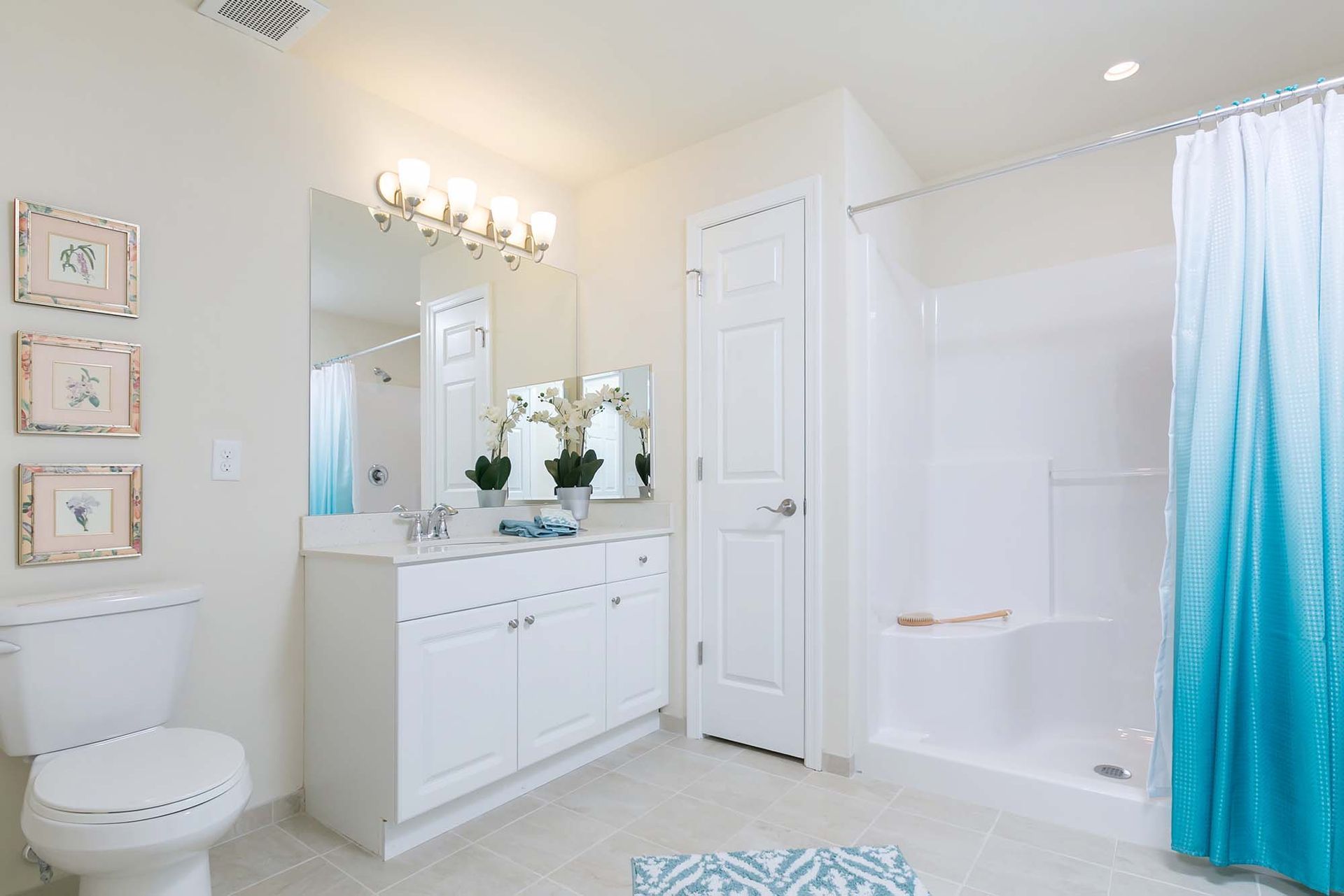 Bright bathroom with white vanity, toilet, and tub/shower with blue curtain.