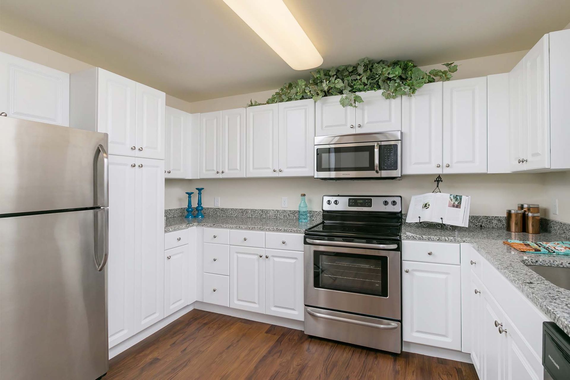 White kitchen with stainless steel refrigerator, oven, microwave, and granite countertops.