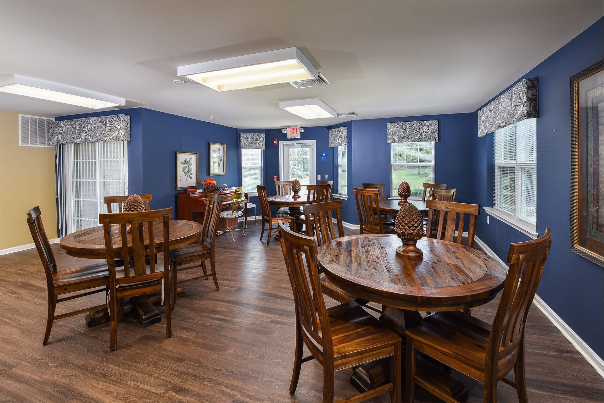 Community lounge with round wooden tables, chairs, and blue walls.