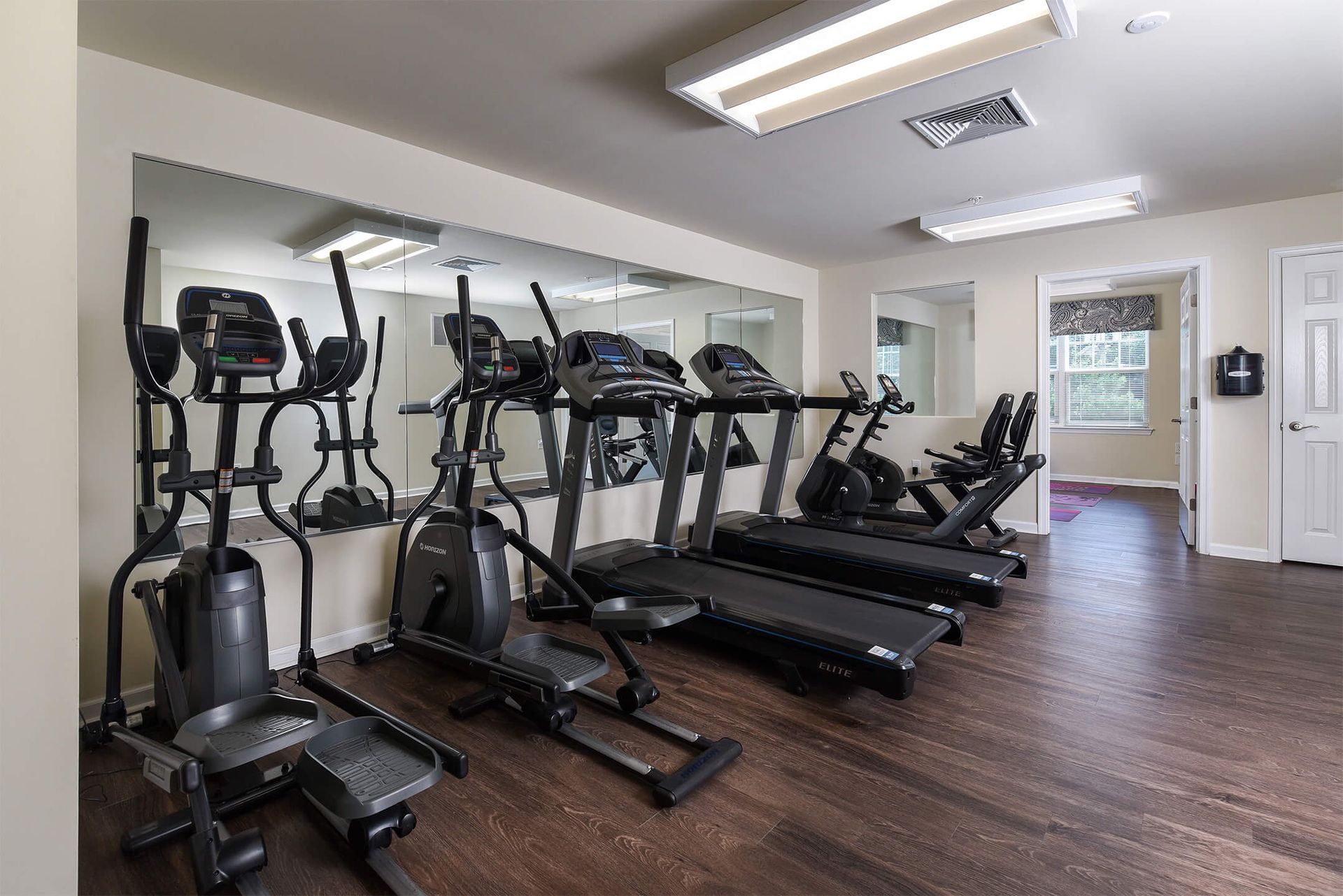 Fitness center with treadmills and elliptical machines along a mirrored wall