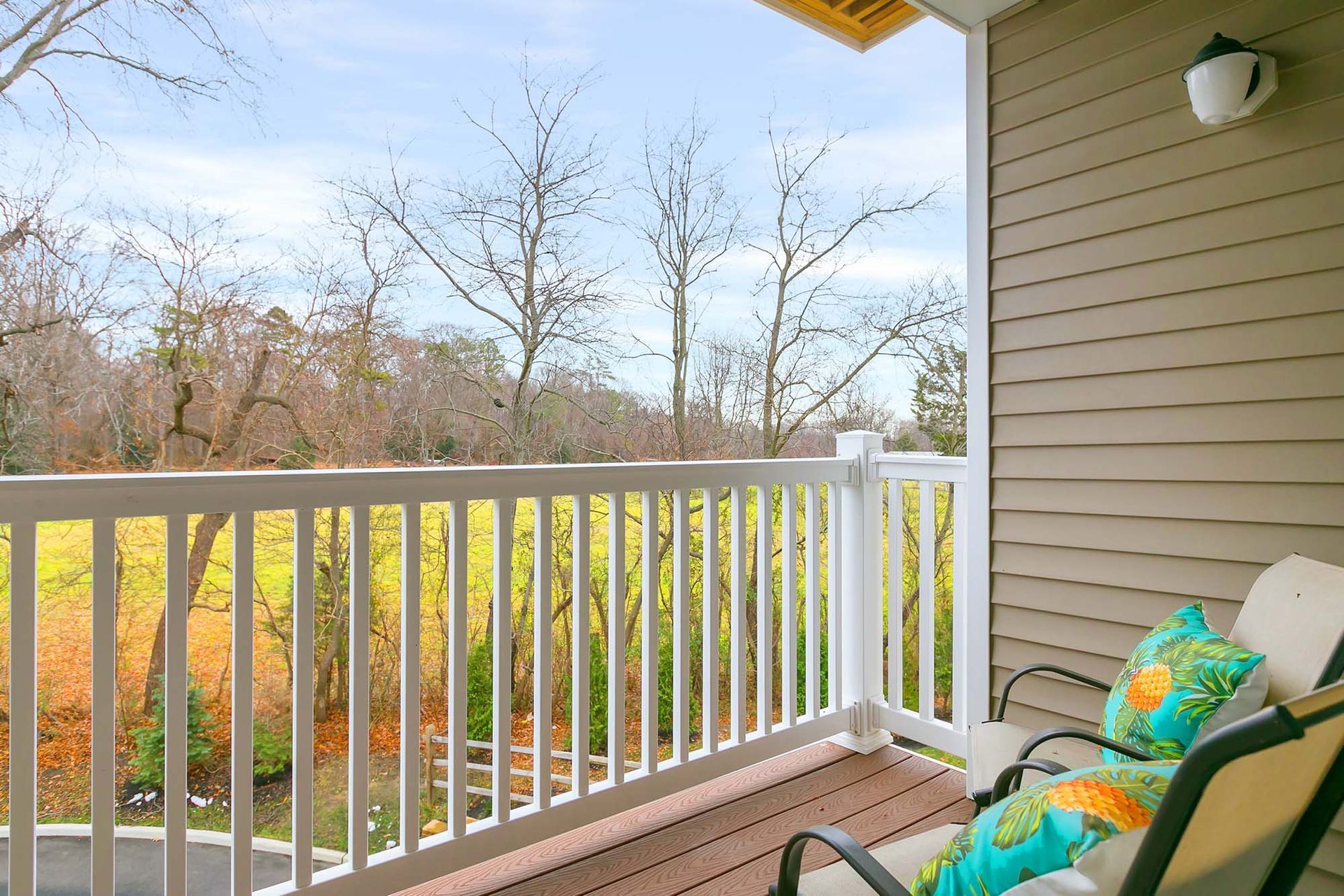 Balcony with white railing and two chairs with turquoise cushions, overlooking bare trees and a lawn.