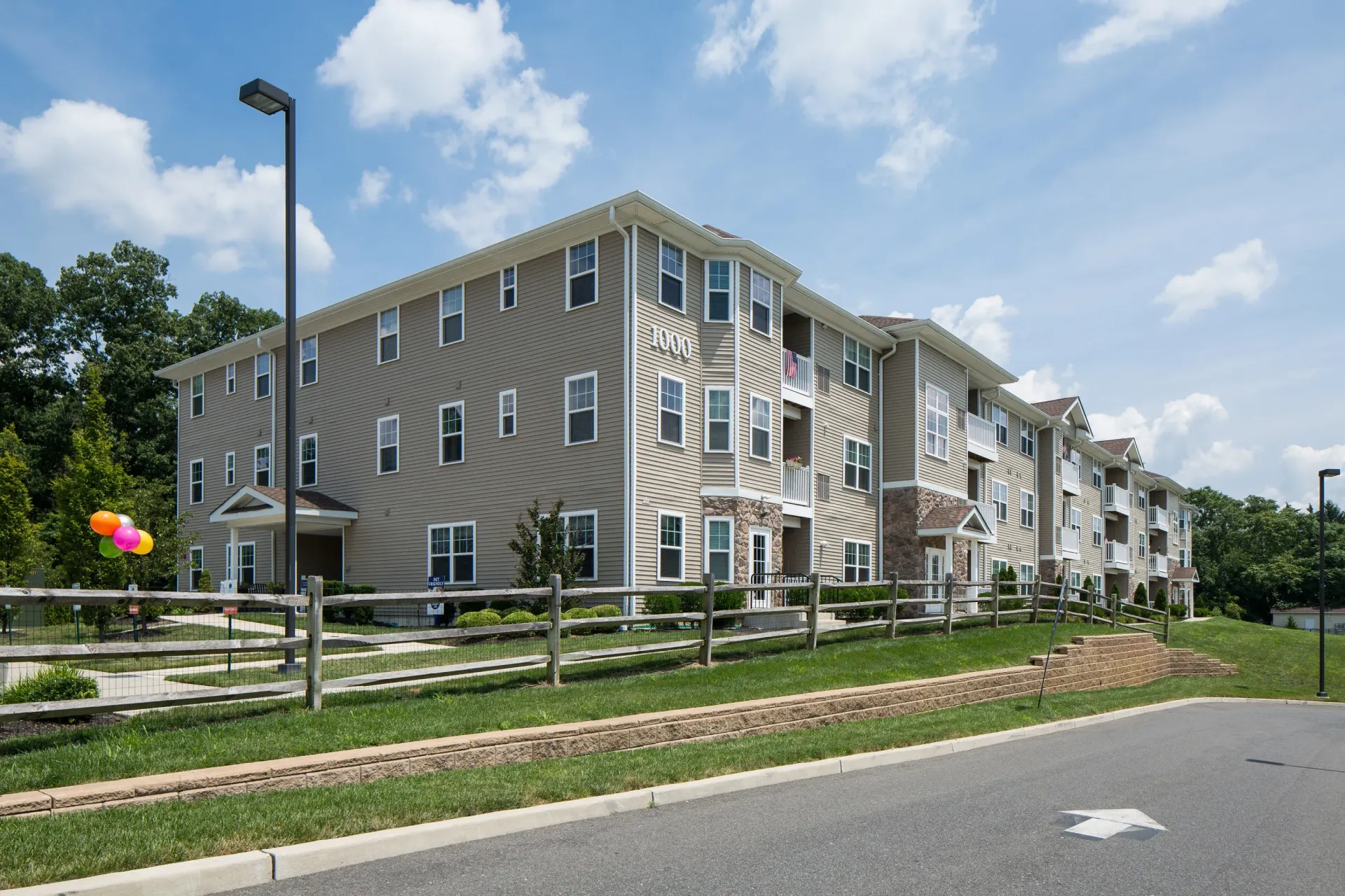 Exterior view of a beige, three-story apartment building with balconies and a wooden fence.