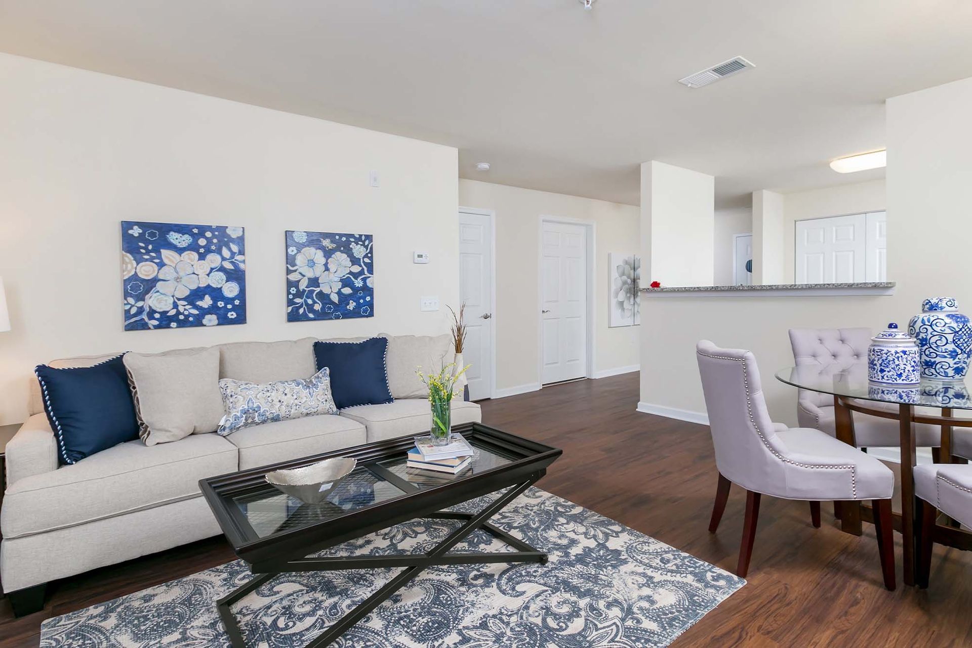 Living room in a modern apartment with a beige sofa, blue cushions, and a glass coffee table.