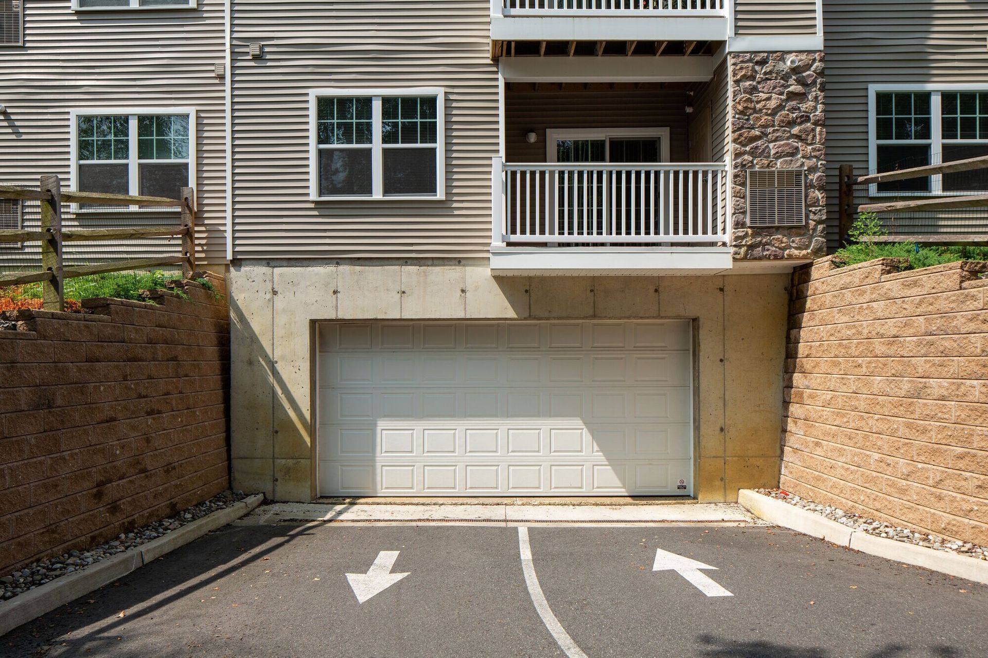 Exterior of a multifamily building showing a ground-level garage door beneath a balcony, with stone and brick accents.