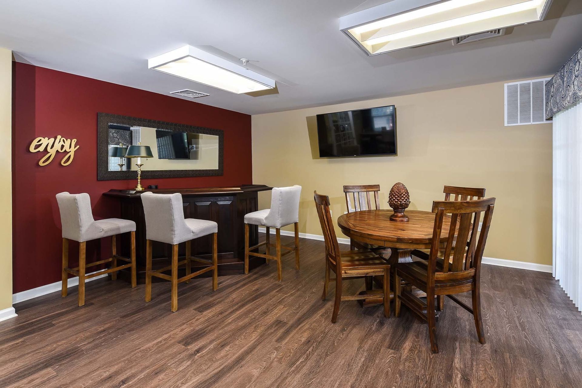 Indoor community lounge with bar-height seating, a round wooden table, and a wall-mounted TV.