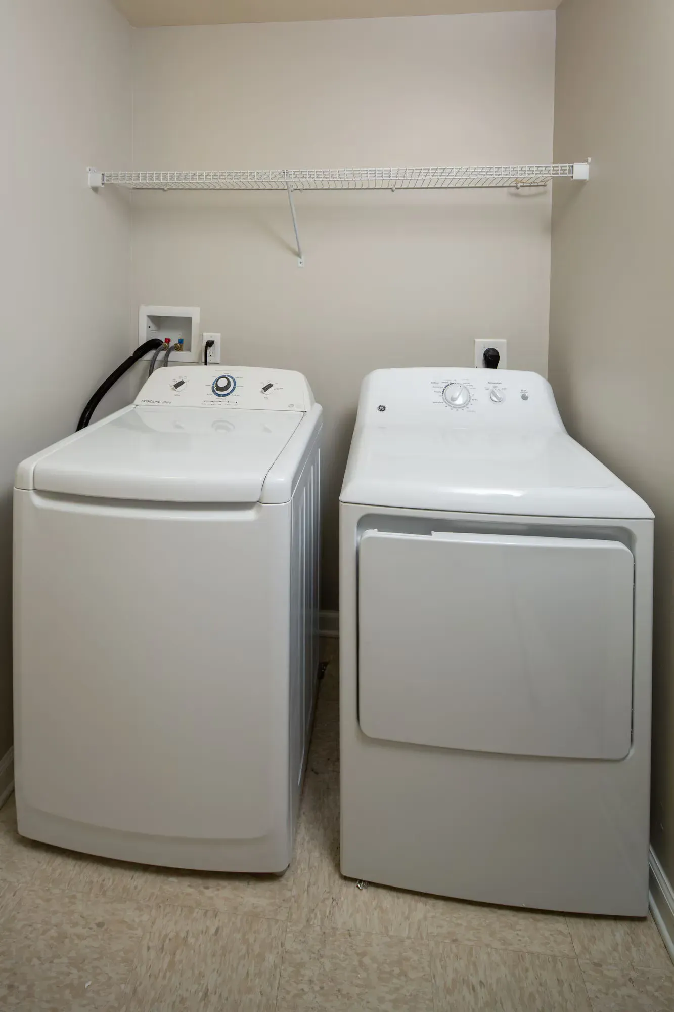 Washer and dryer in a compact laundry closet with a wire shelf above.