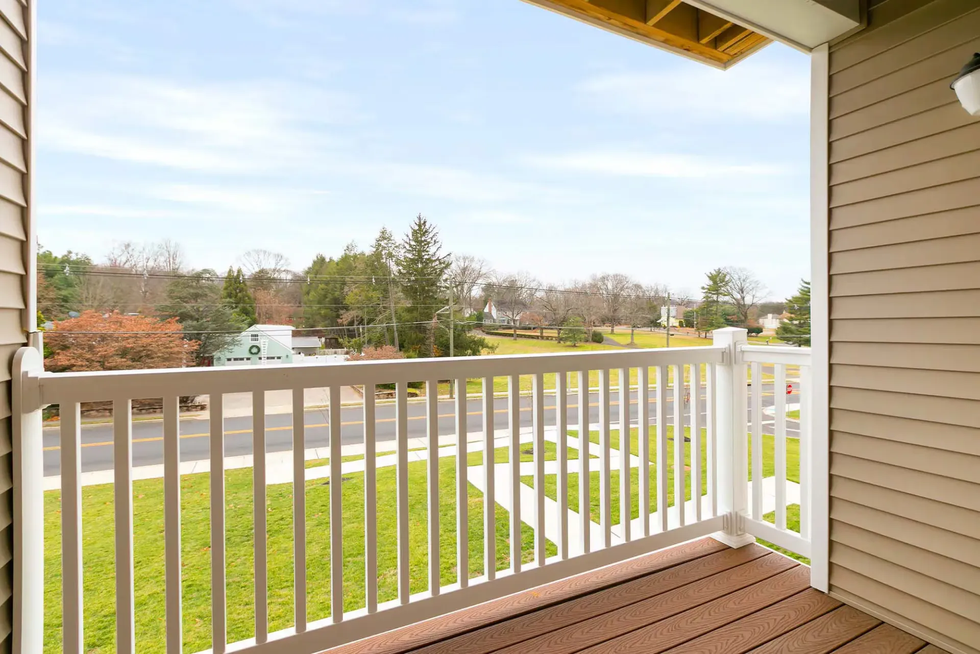 Balcony with white railing and beige siding, overlooking a street and grassy lawn.